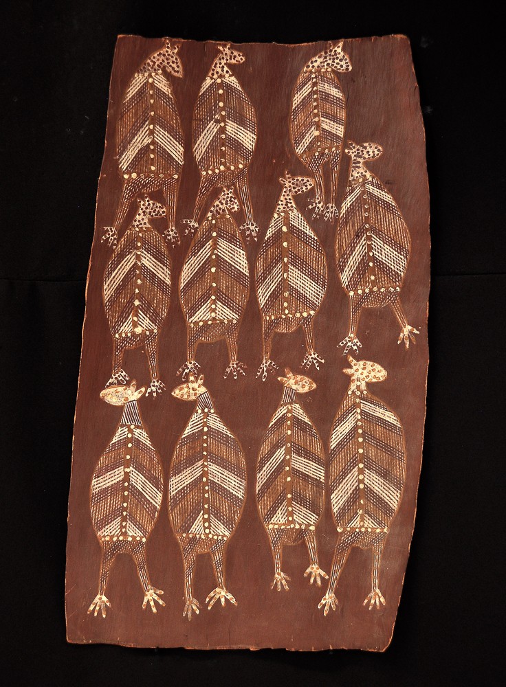 Bark painting by Aboriginal artist Mick Kubarrku featuring twelve stylized flying foxes arranged in a grid pattern. Each figure is adorned with intricate rarrk (crosshatching) in natural ochres of white, yellow, and dark brown, and features dotted accents along the spine and limbs. The animals are depicted in a flat, symbolic style on a reddish-brown bark surface.