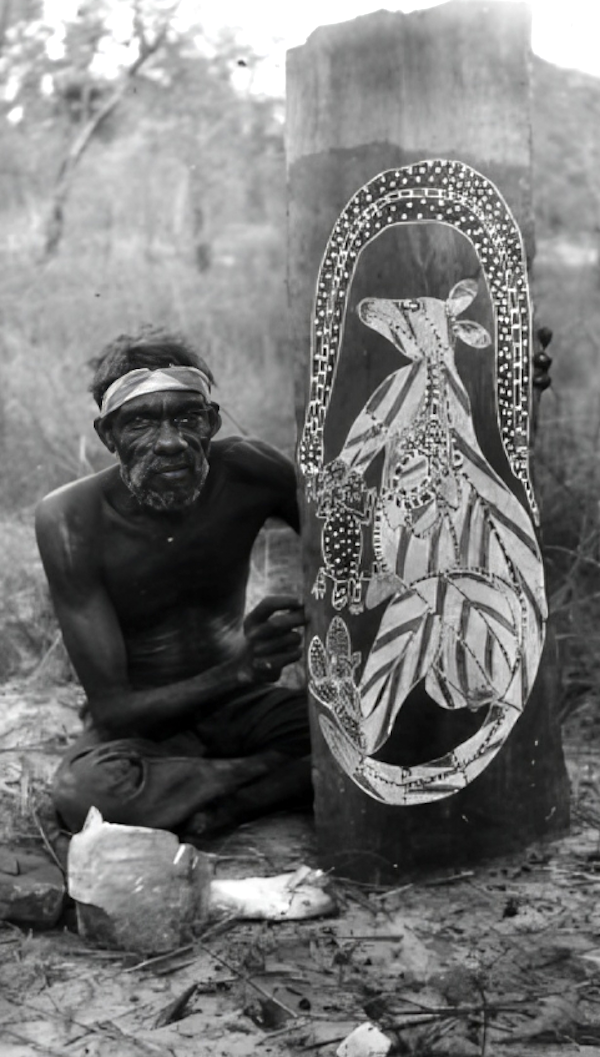 "Aboriginal artist Wally Mandarrk seated beside a bark painting in Arnhem Land, holding a aboriginal bark painting featuring a stylized kangaroo in traditional rarrk (crosshatching) and a depiction of the rainbow serpent, surrounded by bushland."
