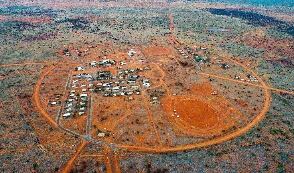 Aerial view of the remote Aboriginal community of Papunya in Central Australia, surrounded by desert landscape and circular road formations.