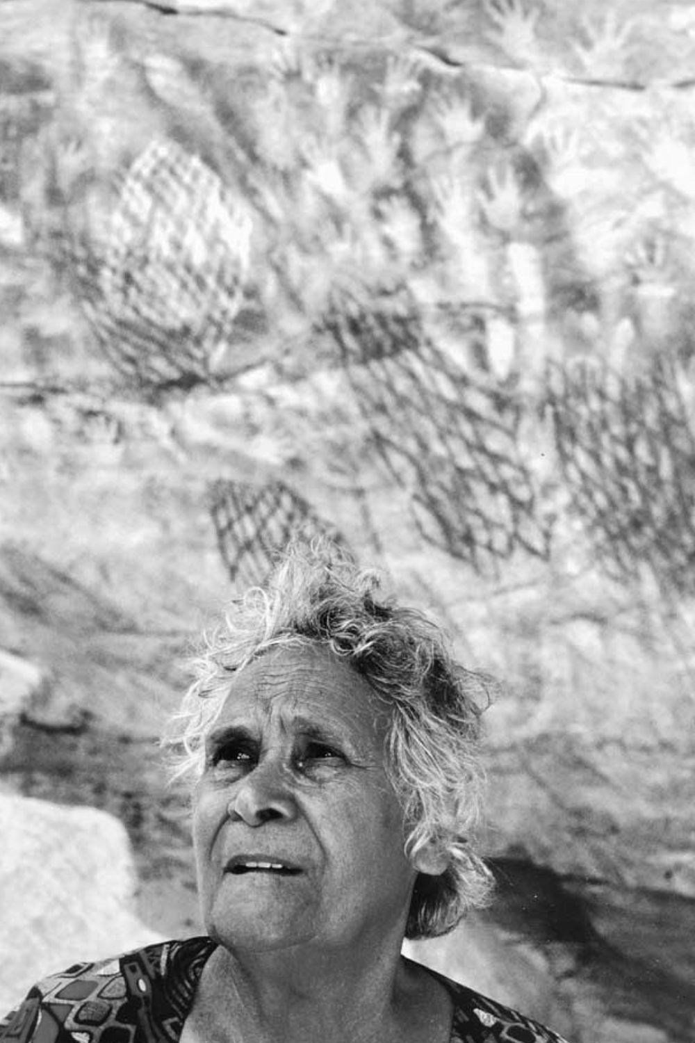 Aboriginal elder standing beneath hand stencils and geometric rock art motifs at Carnarvon Gorge in Central Queensland