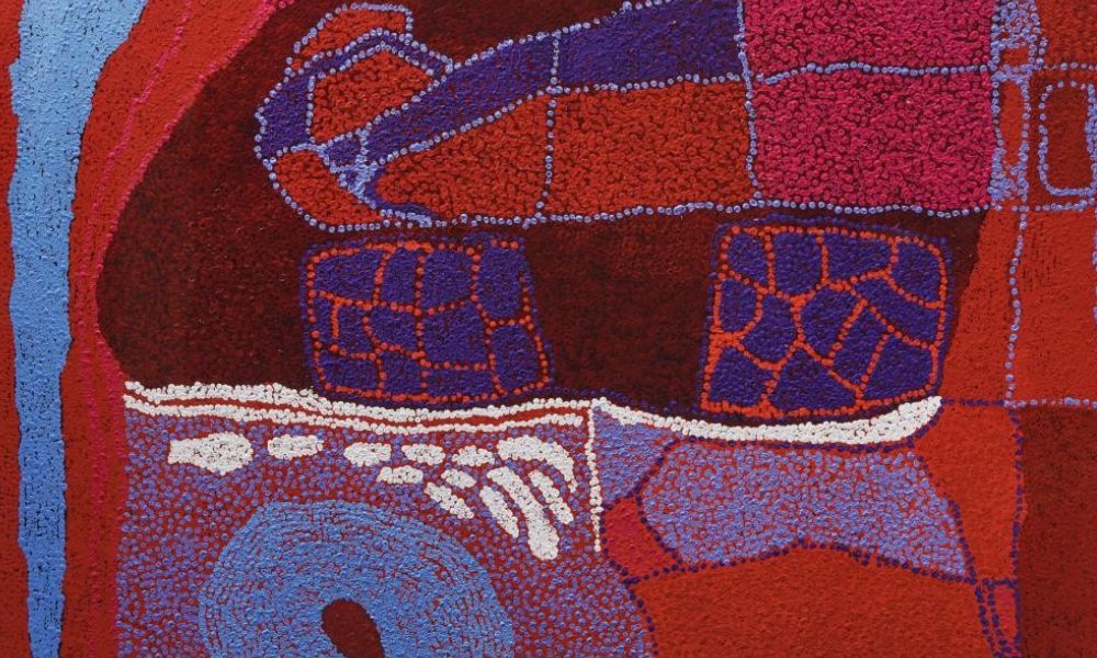 Detail of a painting by Yannima Tommy Watson featuring luminous reds, pinks, purples, and blues arranged in abstract forms representing ancestral Country in the Western Desert.