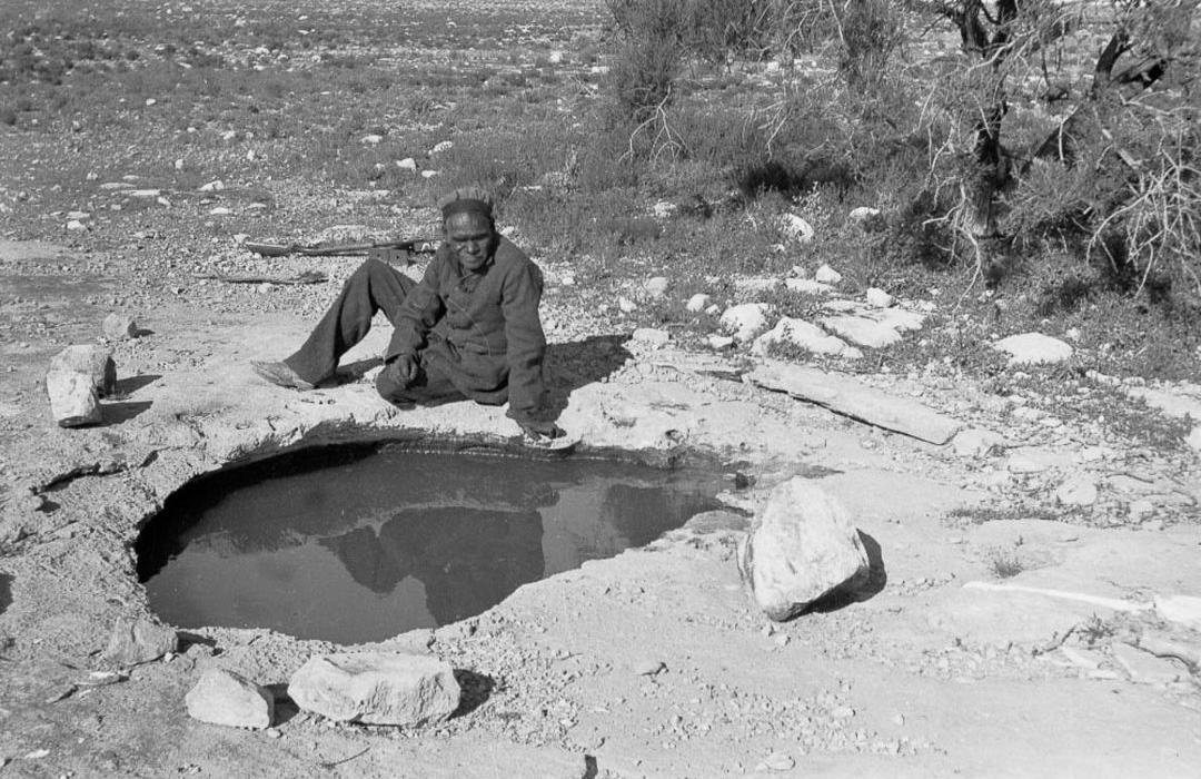 Spinifex elder beside a traditional desert waterhole in the Great Victoria Desert, demonstrating the importance of permanent water sources in Spinifex Country.