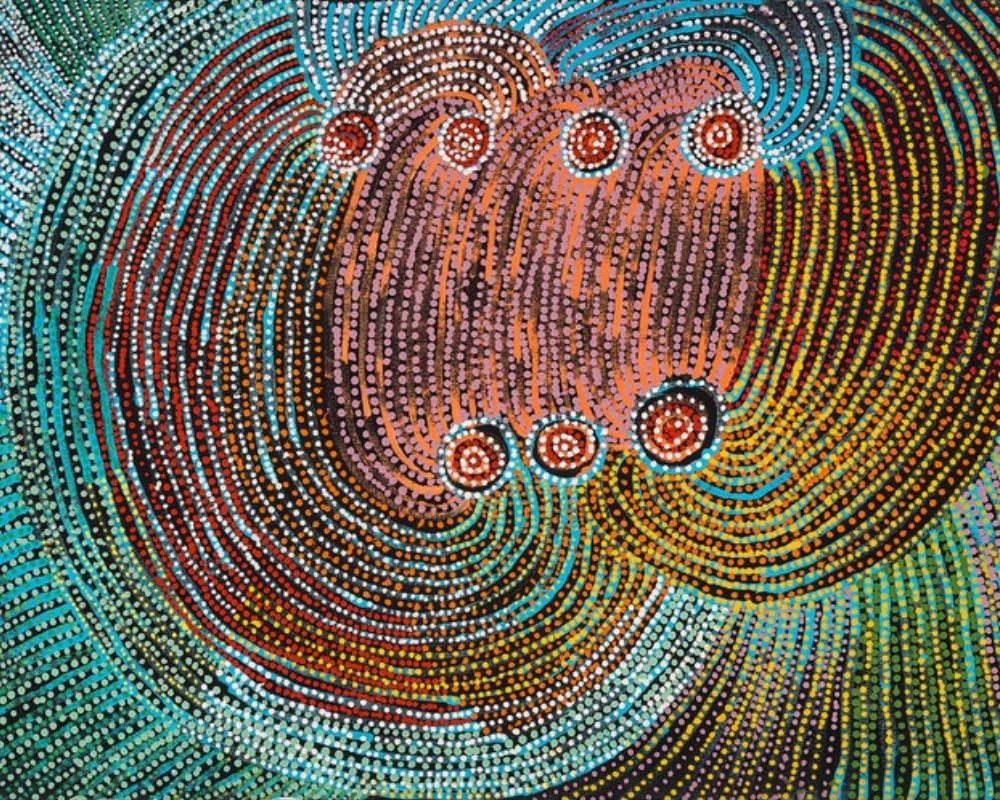 Alt Text: Colourful Aboriginal dot painting by Tommy Mitchell featuring concentric circles, flowing pathways, and vibrant turquoise, pink, orange, and black patterns representing sacred sites in the Western Desert.