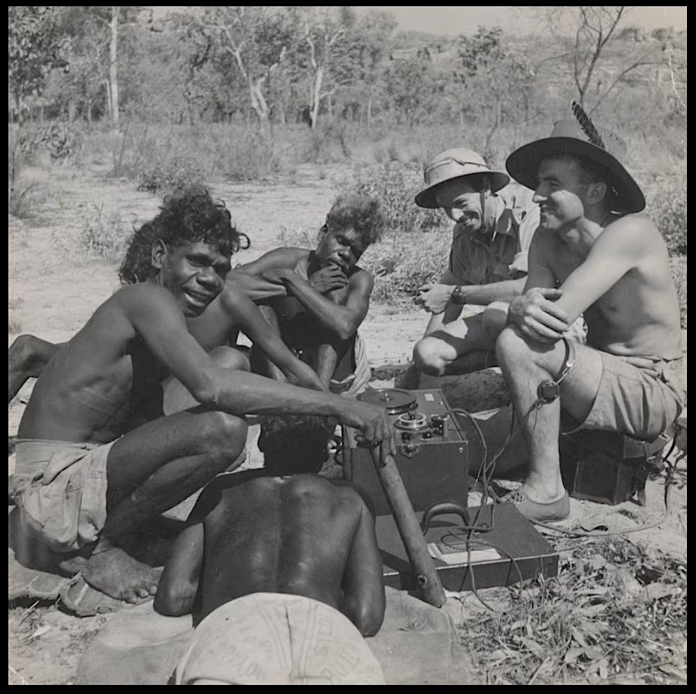 Aboriginal men and members of the 1948 Arnhem Land Expedition gathered around an early field recording machine in Arnhem Land, Northern Territory.