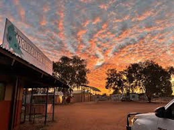 Sunset view of Willowra community in the Northern Territory, showing buildings and red desert streets beneath a dramatic sky in Warlpiri country.