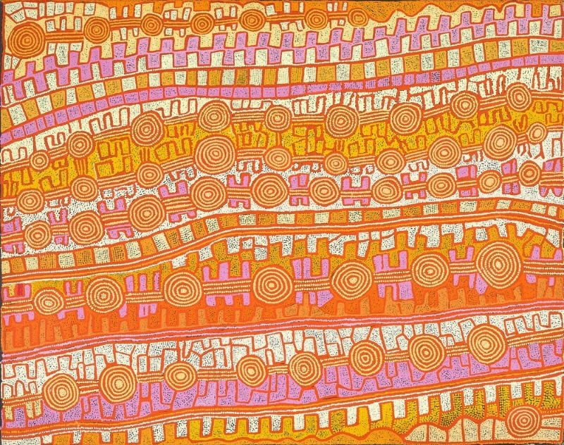 A large horizontal Aboriginal painting glowing with brilliant shades of burnt orange, golden yellow, terracotta, cream, white and soft lilac. The composition is organised into broad, gently curving horizontal bands that sweep across the canvas like parallel sand dunes viewed from above. Within these bands are dozens of concentric circles connected by winding pathways, alternating with repeating stepped motifs and rows of rectangular blocks. Fine white dotted outlines define every shape, while the lilac bands provide vivid contrast against the warm desert colours. Thousands of tiny dots create a shimmering, rhythmic surface that guides the eye from one interconnected ceremonial site to the next, giving the impression of an aerial view of Country shaped by ancestral journeys