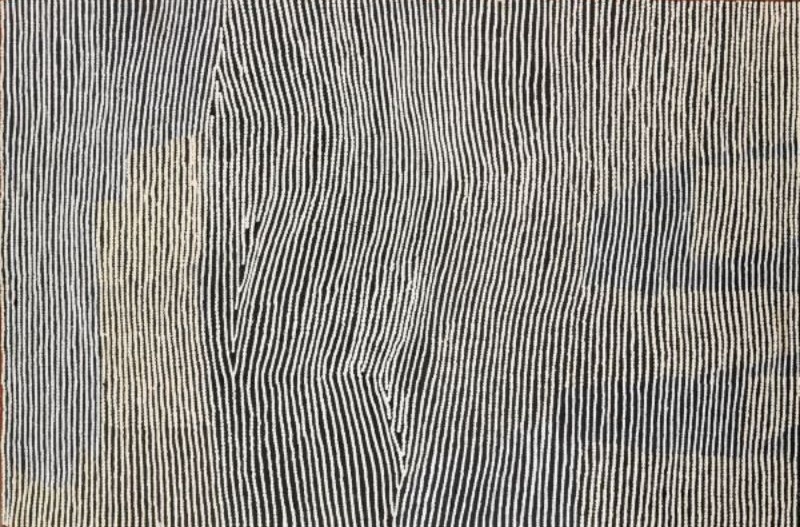 Untitled by Warlimpirrnga Tjapaltjarri, 2003. A vertical painting in black, white and soft grey. Thousands of fine white dotted lines descend across a deep black background in closely spaced vertical bands. The lines gently converge into elongated diamond-shaped forms before flowing apart again, while faint pale grey rectangular passages appear behind the pattern, creating subtle layers and a shimmering sense of depth like light filtering across the desert.