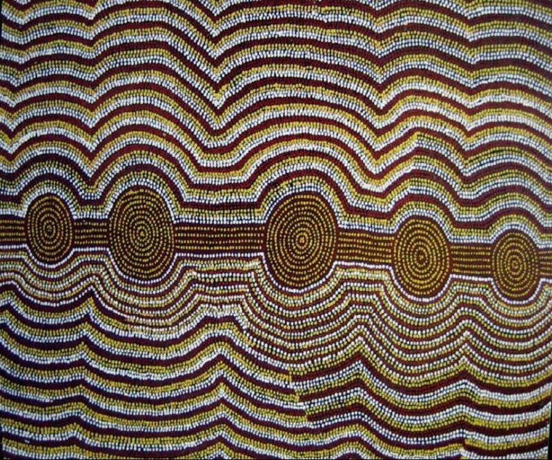Travels of Tingari Men Near Wilkinkarra by Warlimpirrnga Tjapaltjarri, 1993. A tall rectangular painting filled with undulating horizontal bands of tiny white, yellow and reddish-brown dots on a dark brown background. Five concentric circular motifs stretch across the centre, linked by narrow horizontal pathways. The flowing parallel lines create a shimmering optical effect, suggesting movement across the desert landscape.