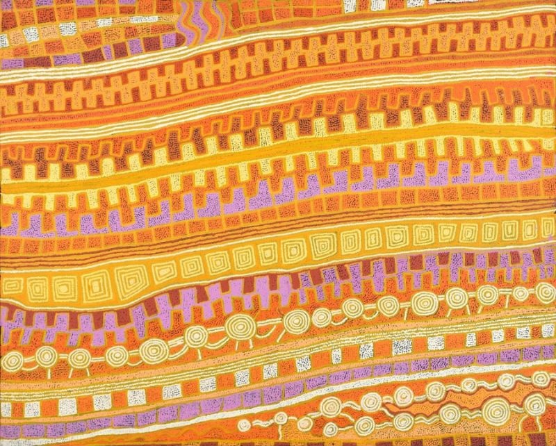 A horizontal Aboriginal painting in radiant desert colours of golden yellow, burnt orange, terracotta, soft lilac, cream and white. Broad parallel bands sweep diagonally across the canvas from left to right like rolling sand dunes viewed from above. Within the bands are repeating stepped motifs, rows of concentric circles linked by winding pathways, and long rectangular forms filled with nested square patterns. Fine white dotted outlines define every shape, while lilac bands provide vivid contrast against the warm oranges and yellows. Thousands of tiny dots create a shimmering surface that gives the painting a strong sense of rhythm, movement and depth, evoking an aerial view of interconnected ceremonial sites and ancestral travelling routes across the Western Desert.