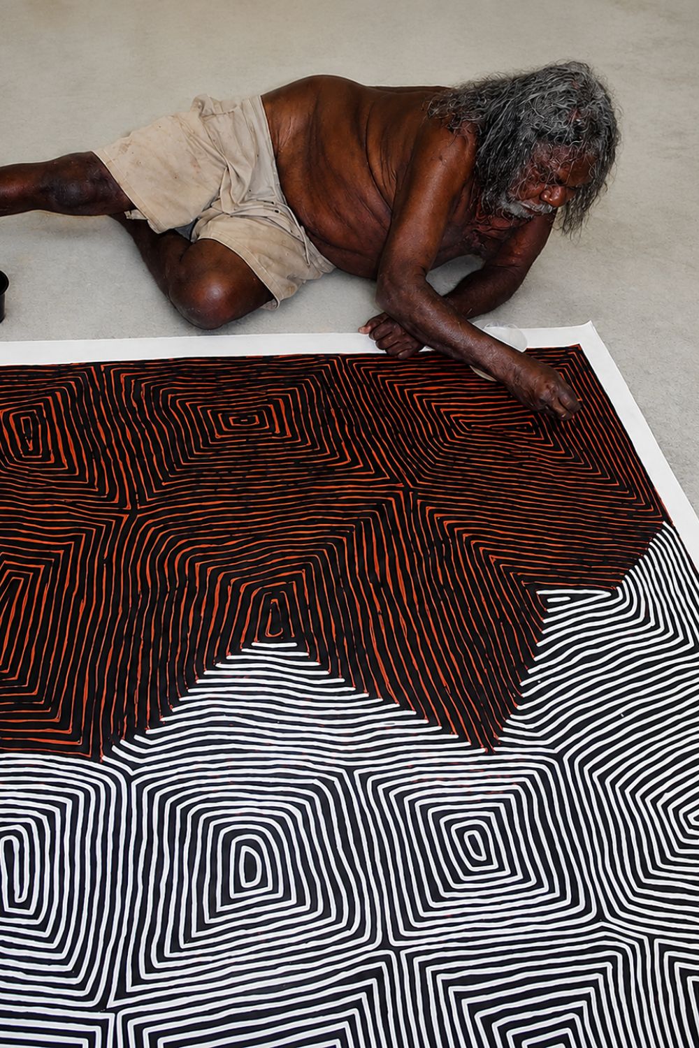 George Tjungurrayi painting one of his signature Tingari compositions, applying the meticulously controlled parallel lines that became the defining feature of his mature style.