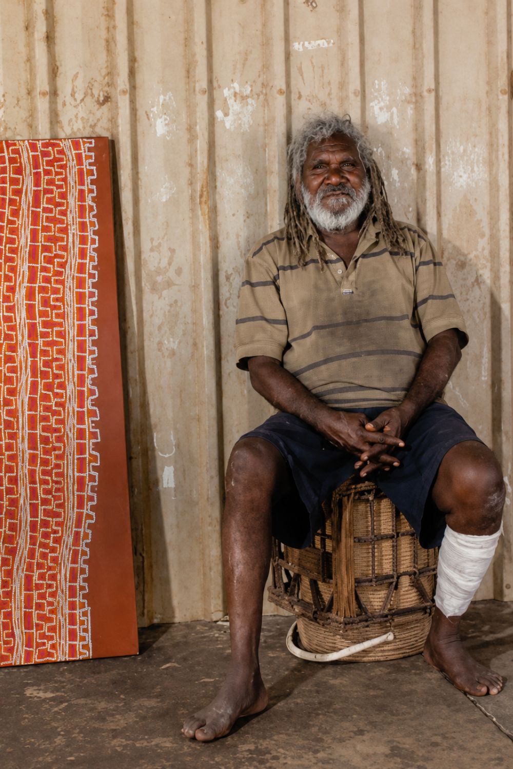 Patrick Tjungurrayi seated beside one of his geometric Tingari paintings at an art centre in the Western Desert.