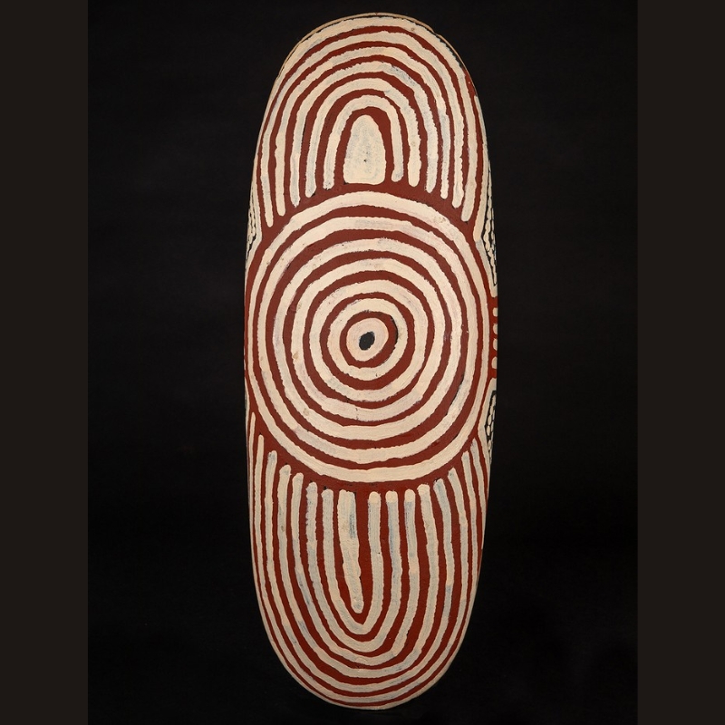 Ronnie Tjampitjinpa Men's Ceremony 2005 painted beanwood shield, with a central concentric circle and elongated white and red ochre ceremonial designs above and below.