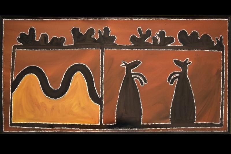 Rover Thomas ceremonial board showing a yellow double-peaked form, two upright black kangaroo-like figures and dark rock shapes outlined with white dots on an ochre ground.