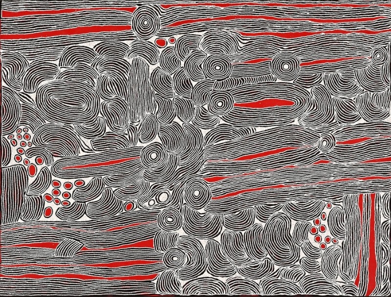 Monumental black, white and red Aboriginal painting by Ningura Napurrula filled with dense fields of fine parallel lines. Concentric circles are scattered across the composition among overlapping rounded forms, while long horizontal and elongated shapes contain vivid red channels. Small clusters of red and white ovals punctuate the predominantly black-and-white surface.