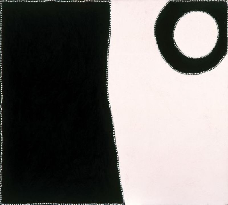 Minimalist Aboriginal painting divided vertically into two unequal sections. The left side is a large solid black rectangle, while the right side is a pale cream field containing a single black ring near the upper right corner. Fine white dots outline the outer border, the central dividing line and the circular form, creating a stark contrast between the black and cream areas.