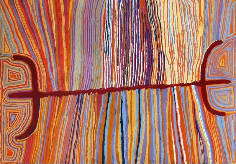 Judy Watson Napangardi painting with hundreds of vertical lines in orange, red, yellow, blue, purple and white crossed by a dark red horizontal line connecting large semicircular forms at either side.