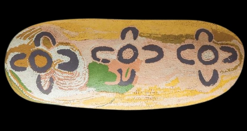 Oval wooden coolamon painted by Maggie Watson Napangardi with dark circular and U-shaped motifs across a pale yellow, pink, green and white dotted ground.