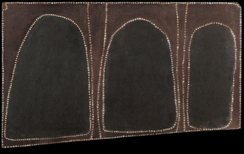 Rover Thomas ochre painting with three large irregular black forms outlined in white dots and separated by narrow vertical brown bands.