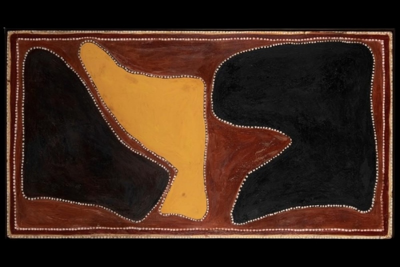 Rover Thomas ochre painting with two large irregular black forms flanking a central yellow shape, all outlined with white dots on a red-brown ground.