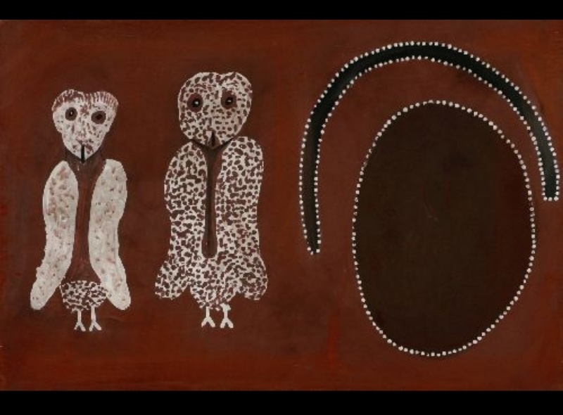 Rover Thomas ochre painting showing two white owl-like figures beside a large dark oval and curved black band outlined with white dots on a red-brown ground.