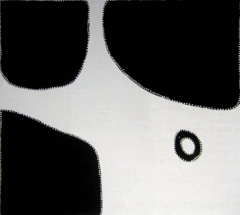 Minimalist Aboriginal painting with a pale cream background crossed by a broad winding white pathway between four large black shapes. Three black rounded blocks occupy the upper left, upper right and lower left corners, while a small black ring with a white centre appears near the lower right. Fine white dots outline every black form and the outer border, creating strong contrast between the black and cream areas.