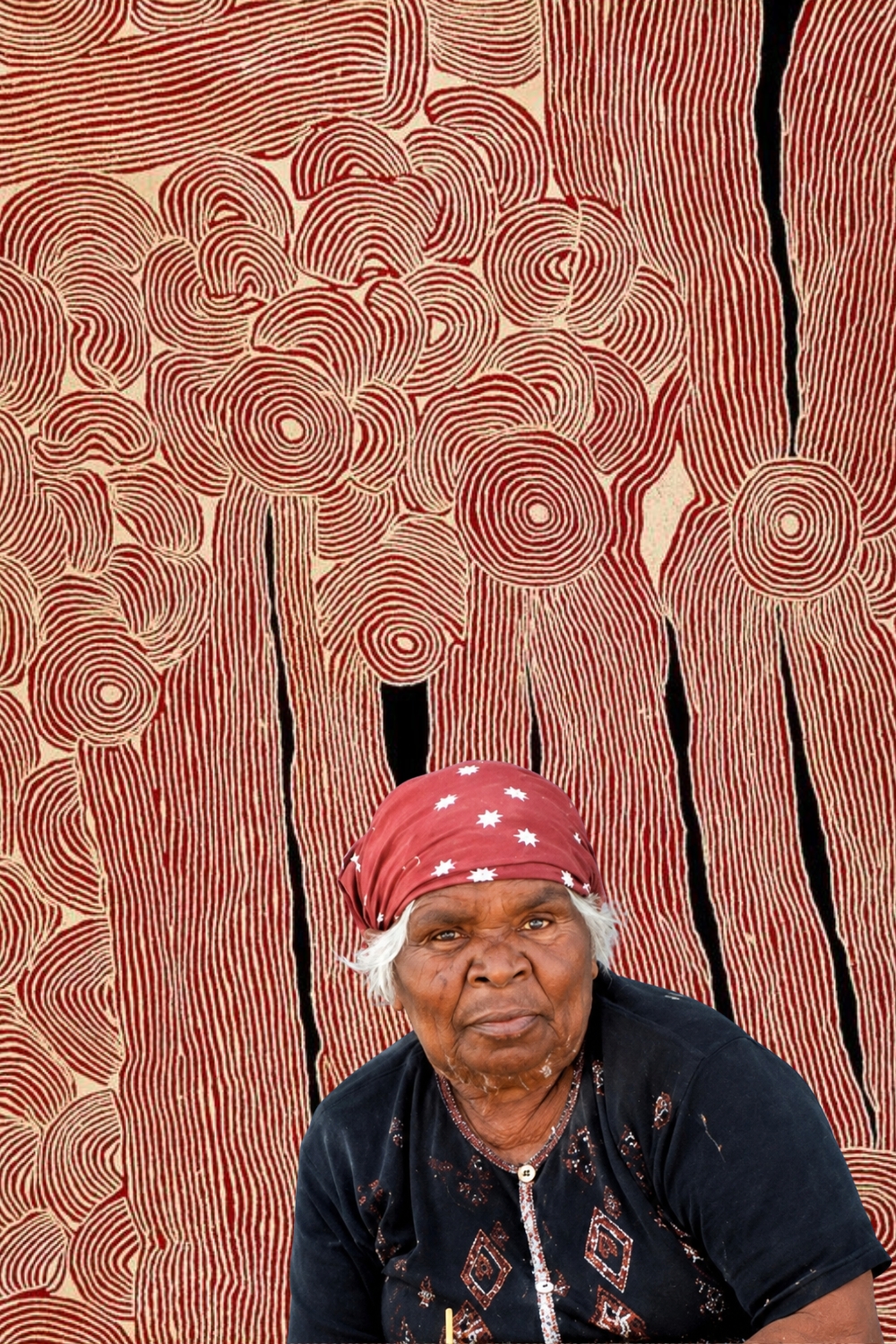 Pintupi artist Ningura Napurrula Gibson seated in front of one of her distinctive red and white paintings.