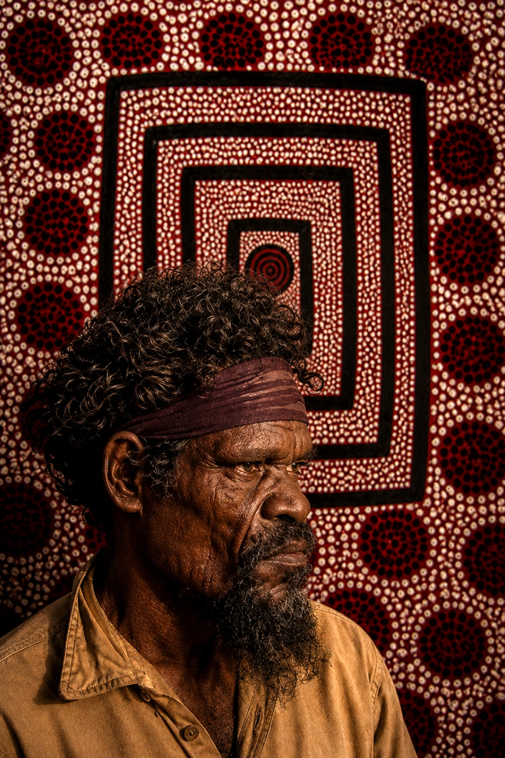 Portrait of Pintupi artist Anatjari Tjakamarra with a Western Desert painting in the background