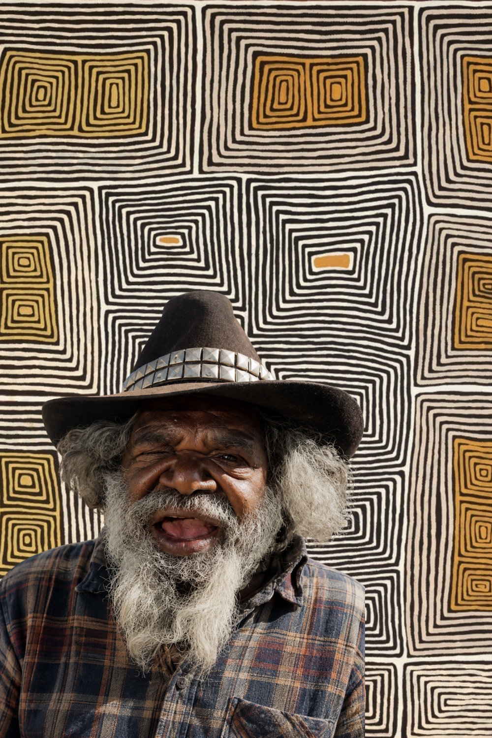 Portrait of Ronnie Tjampitjinpa in front of one of his geometric Tingari paintings, celebrated Pintupi artist from Kintore.