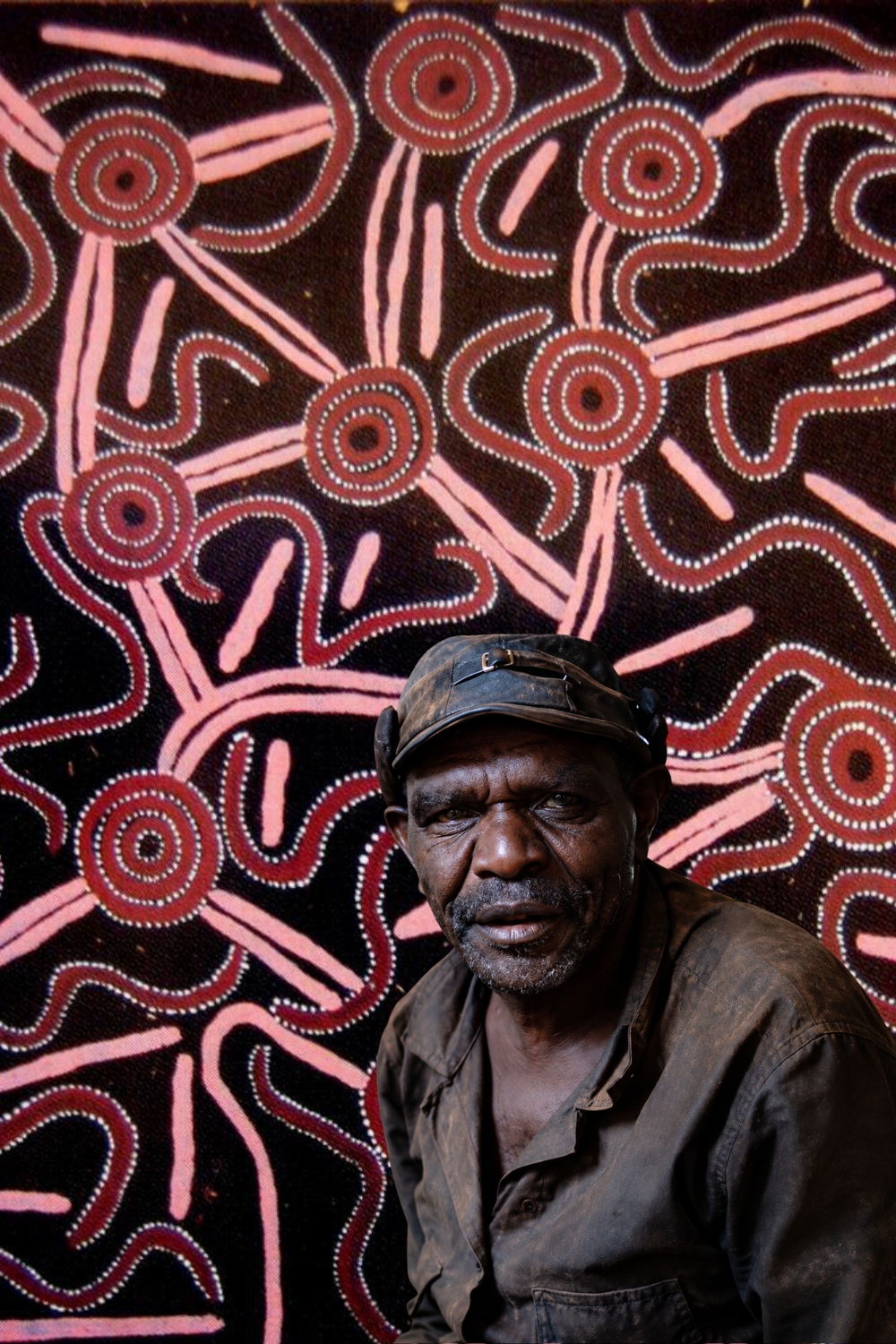 Portrait of Pintupi artist Charlie Tawara Tjungurrayi with a Western Desert painting in the background