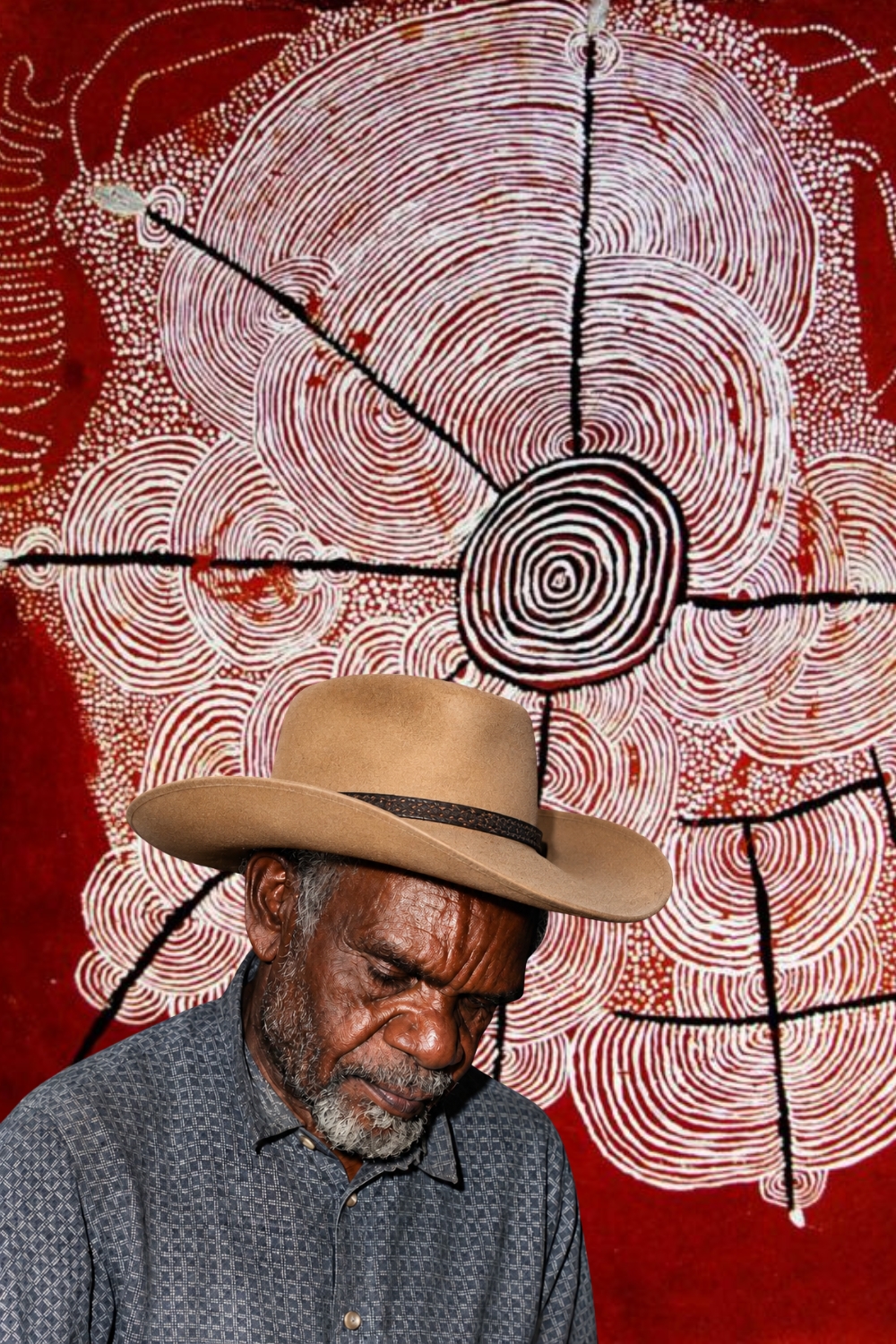 Pintupi artist Shorty Lungkata Tjungurrayi with a Western Desert painting featuring concentric forms, radiating lines and dense dotting.