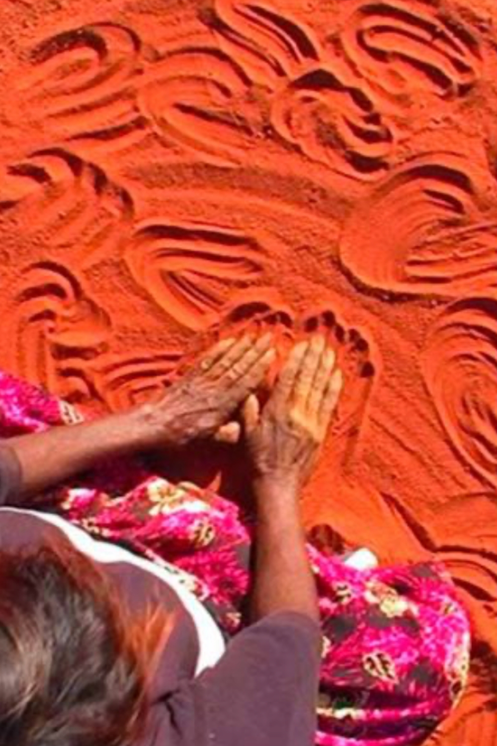 Aboriginal women creating traditional designs by drawing patterns in red desert sand