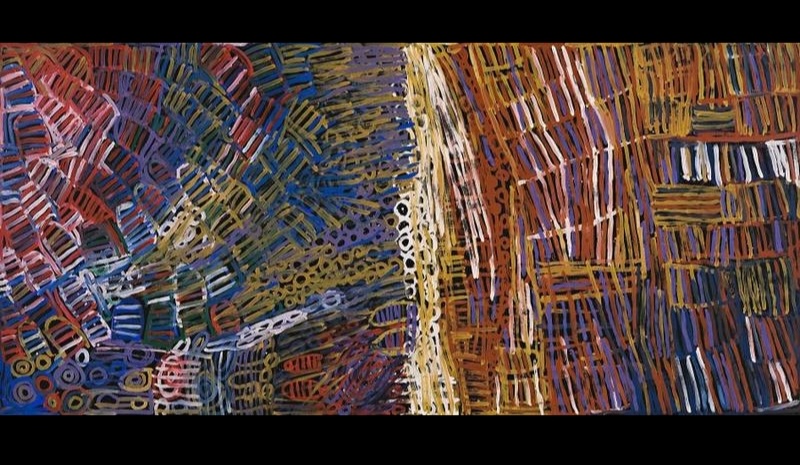 Large Minnie Pwerle painting filled with dense overlapping striped and circular forms in blue, red, purple, ochre, white and pink, arranged across a dark background.