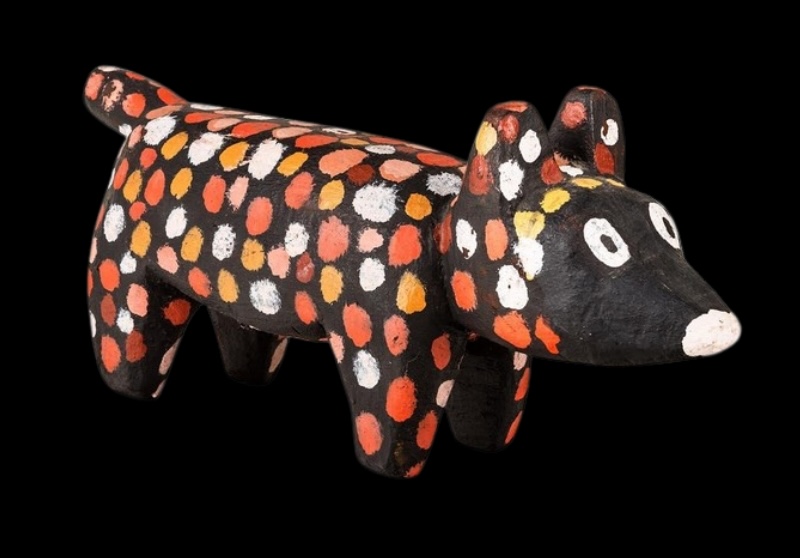 Carved wooden puppy by Angelina Pwerle, painted black with large red, orange, yellow and white dots across its body.