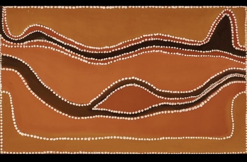Rover Thomas painting in orange and golden-brown ochre crossed by two long, winding dark brown forms. The upper band snakes horizontally across the canvas and rises sharply near the right edge, while a broader curved band below loops around a narrow pointed shape. Rows of large white dots outline the dark forms and frame the painting.
