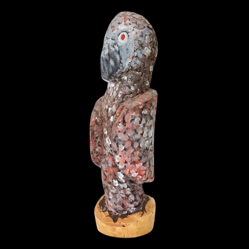 Carved wooden Night Owl by Angelina Pwerle, with a rounded grey head, red and white eye and mottled red, white, grey and black body.