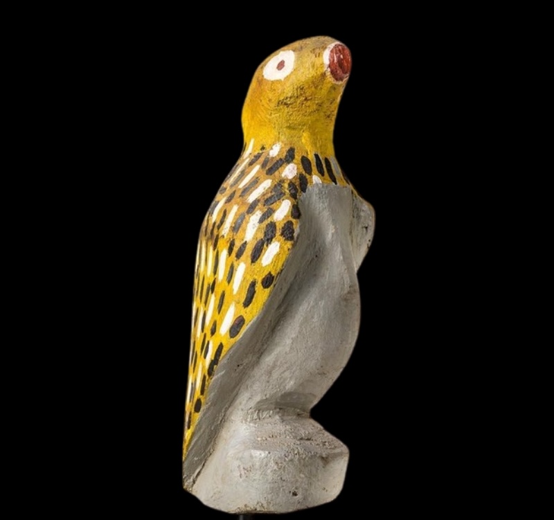 Carved wooden wren by Angelina Pwerle, painted yellow and grey with black and white markings across its back and wings.
