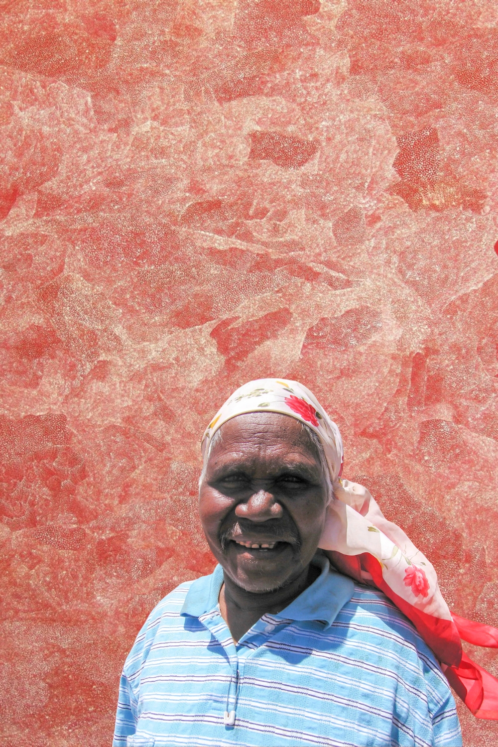 Angelina Pwerle Ngal standing in front of one of her densely patterned Aboriginal paintings.