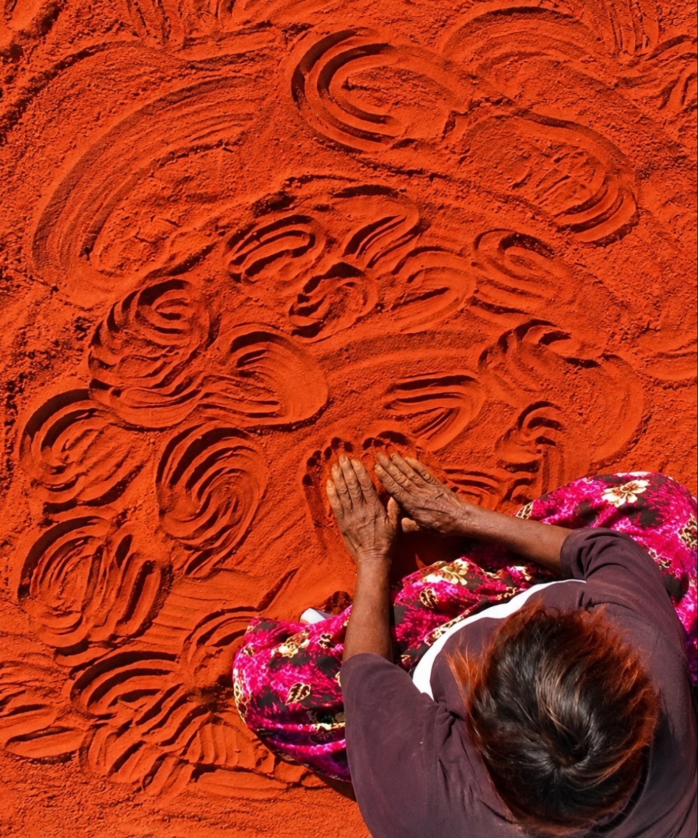 Aboriginal woman creating traditional designs with her hands in red sand