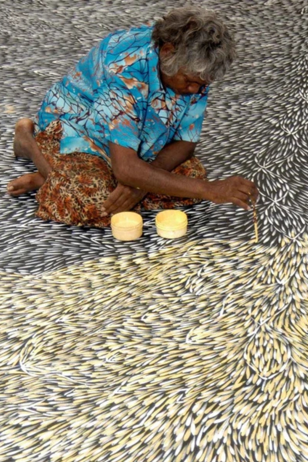 Gloria Petyarre seated on a large canvas, painting flowing Bush Medicine Leaves with a fine brush.