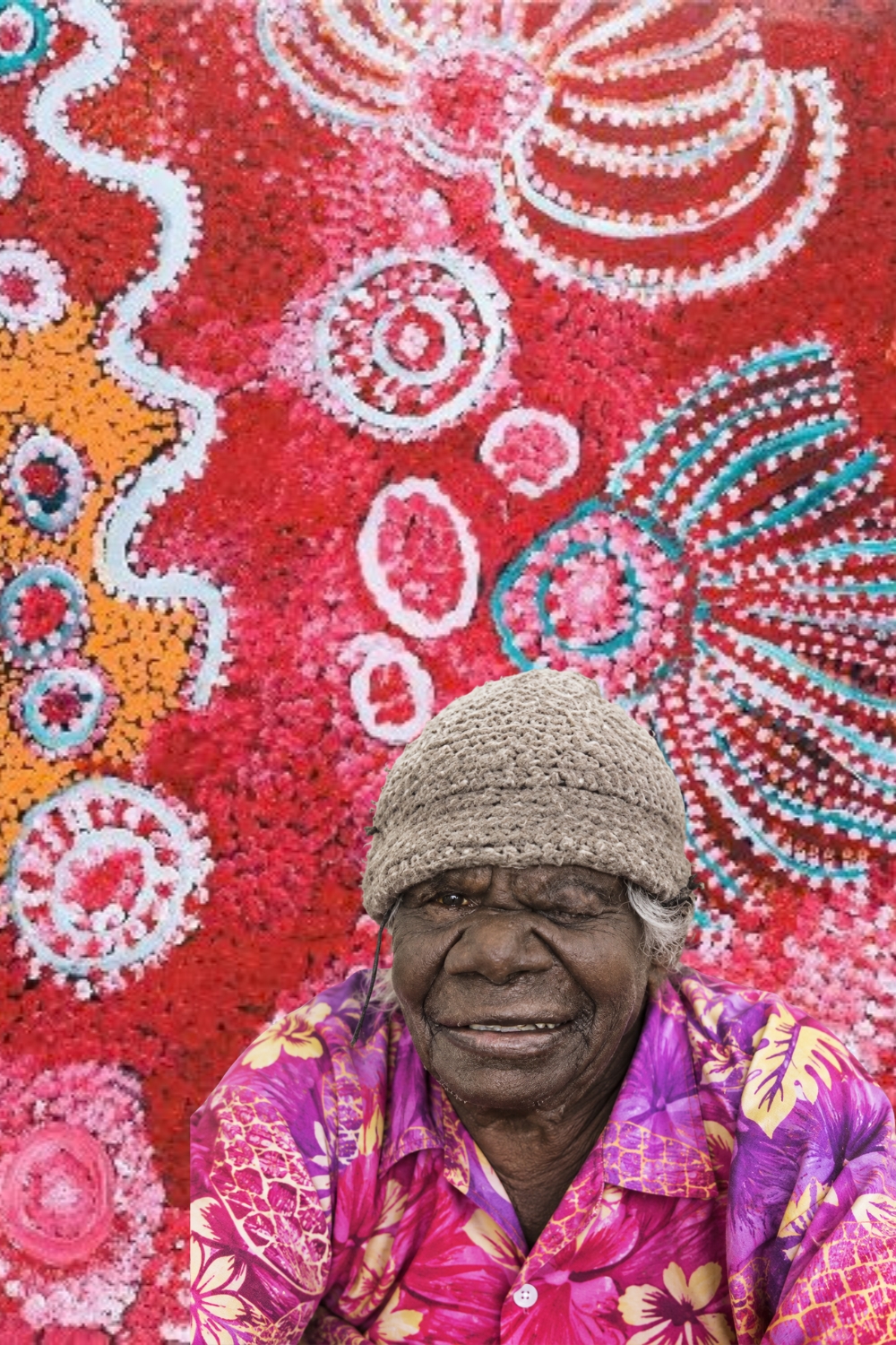 Wingu Tingima seated in front of one of her colourful Western Desert paintings