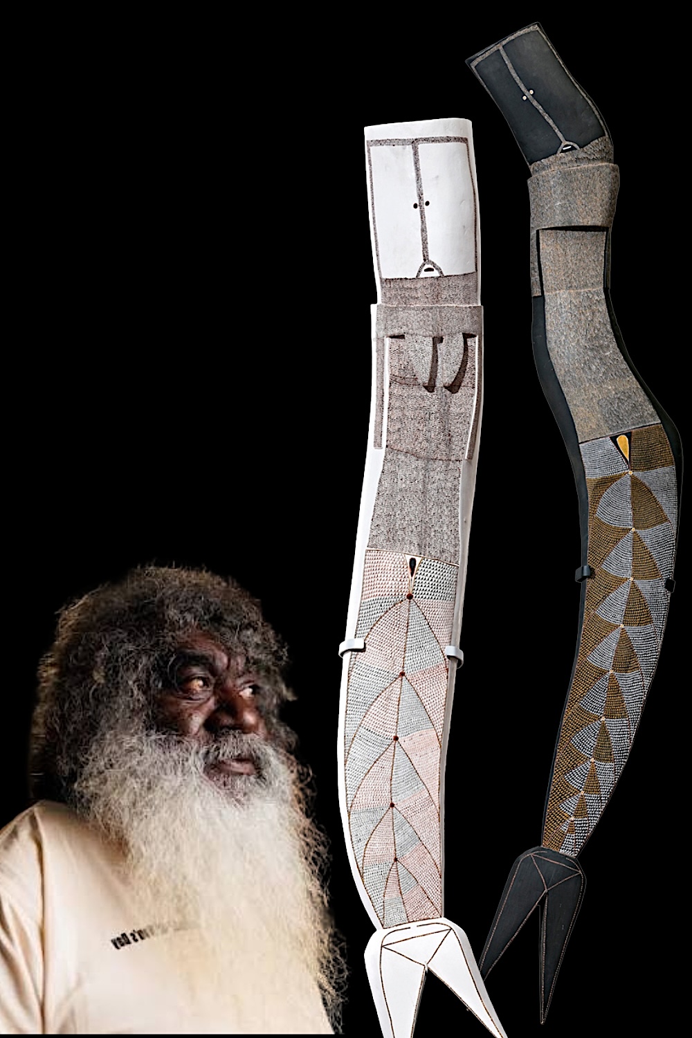 Owen Yalandja, western Arnhem Land Aboriginal artist, pictured beside two tall carved wooden Yawkyawk spirit sculptures decorated with intricate painted scales.