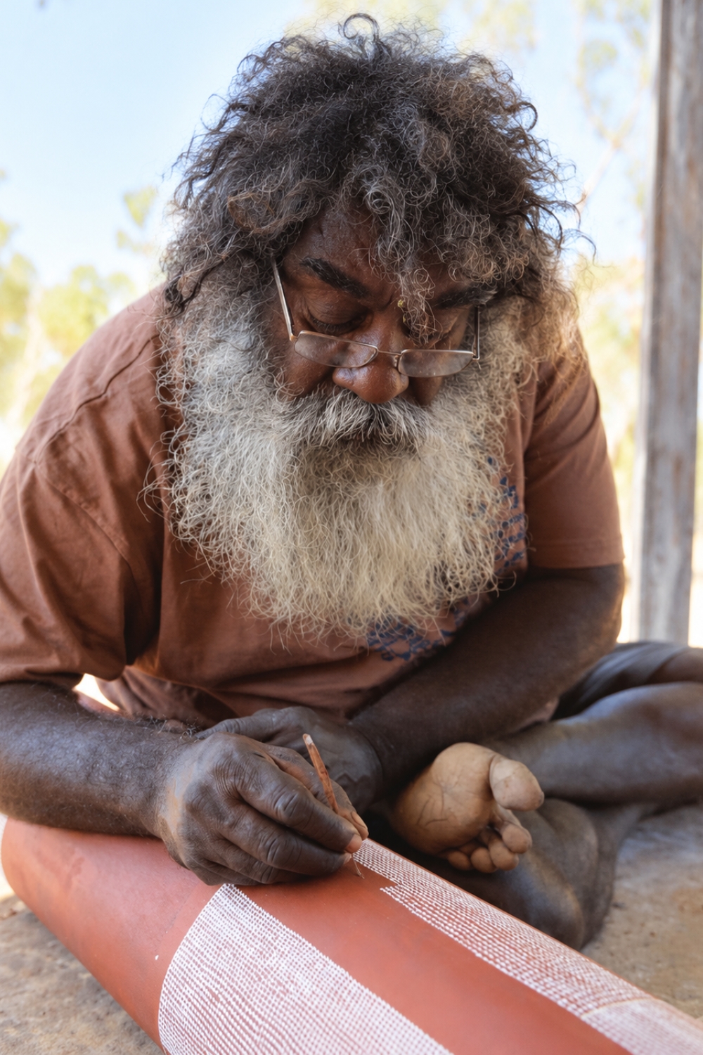 Kuninjku Aboriginal artist Owen Yalandja painting fine white scale patterns onto a carved wooden Yawkyawk sculpture in western Arnhem Land.